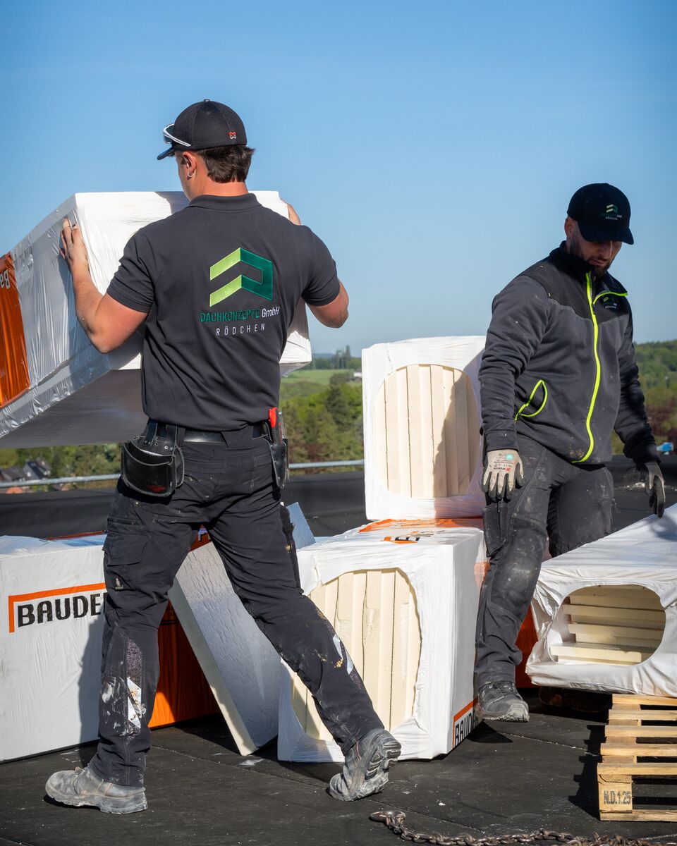 Zwei Dachdecker tragen Dämmplatten über ein Flachdach