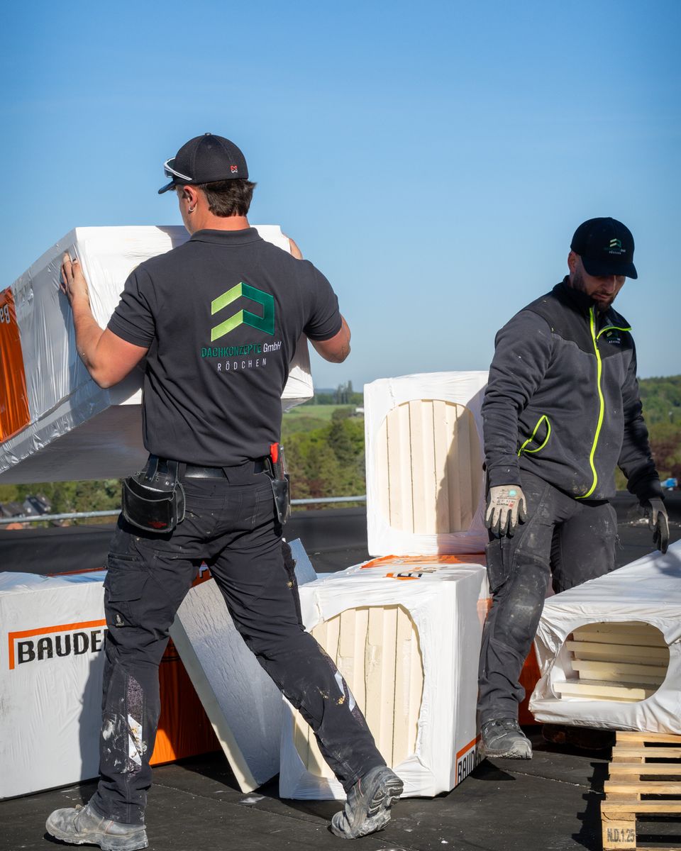 Zwei Dachdecker von DACHKONZEPTE tragen Dämmplatten über ein Flachdach